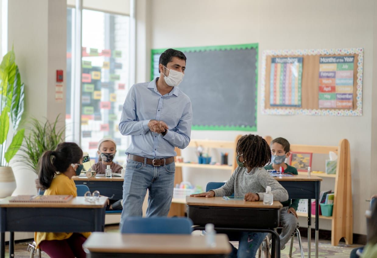 color photograph of a male teacher wearing a face mask in an elementary school classroom