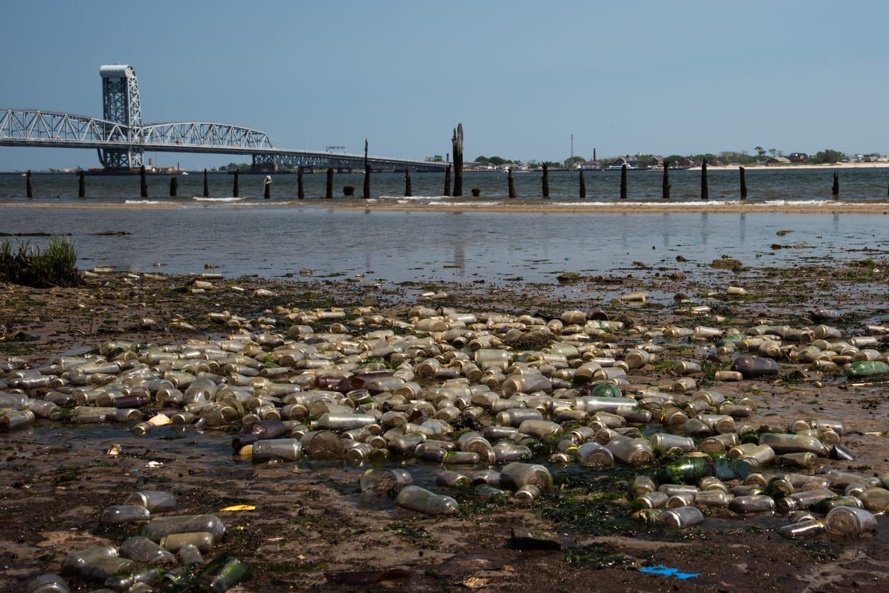 color photograph of a polluted shore with bottles and other trash littering the sand.