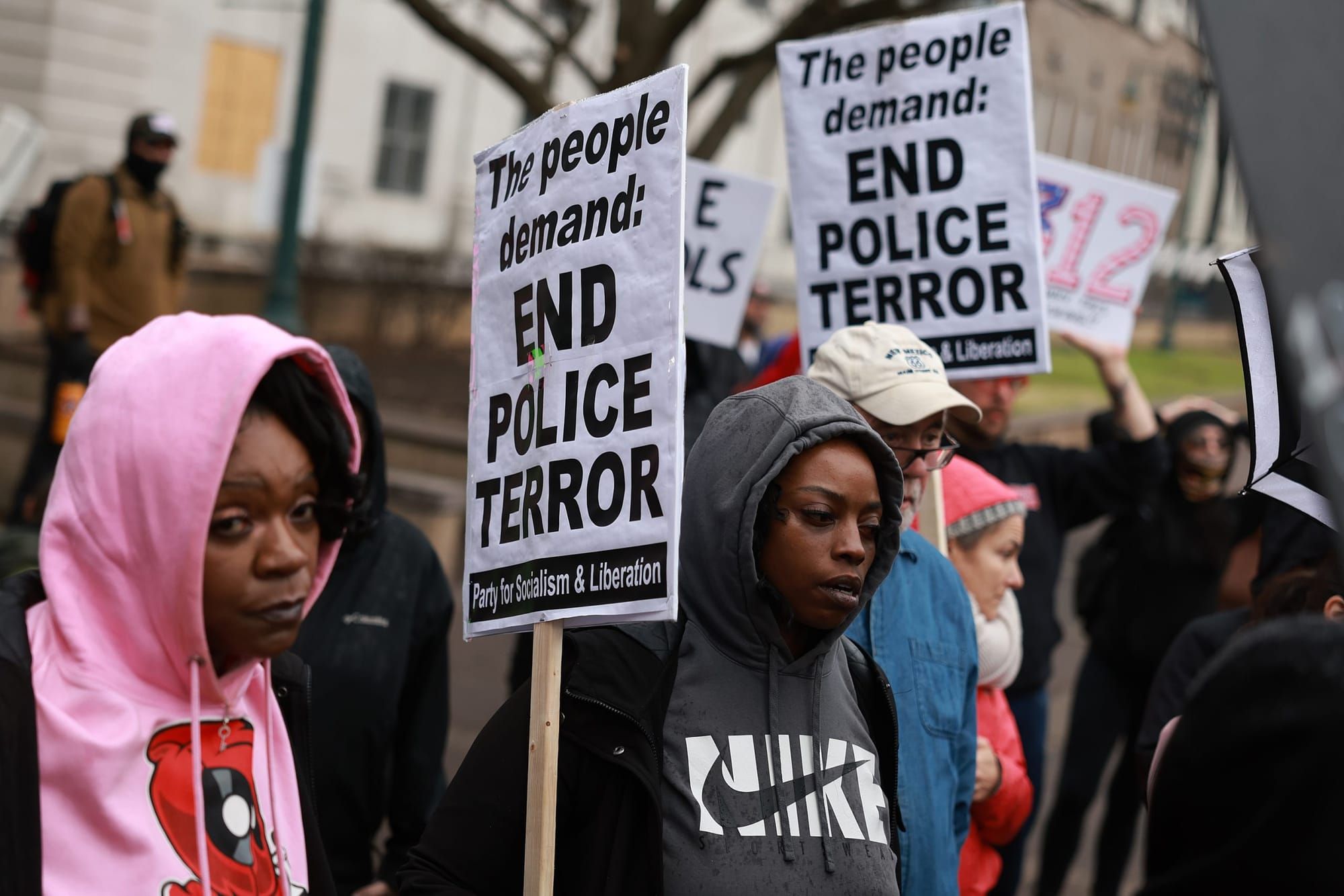 color photograph of an outdoor protest. people hold picket signs that read "end police terror"