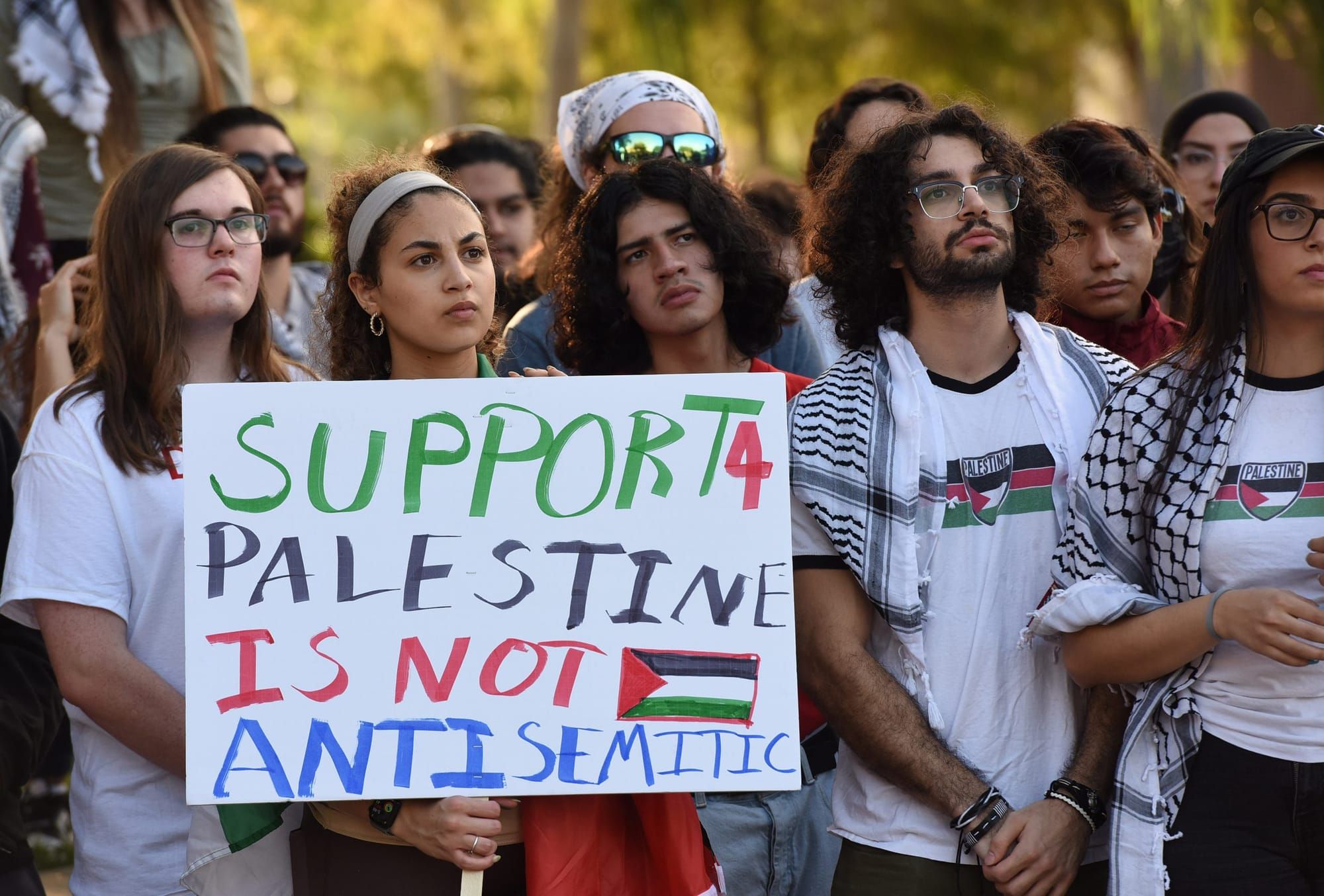 color photograph of an outdoor protest in support of palestinian liberation. someone in the foreground holds a white poster w
