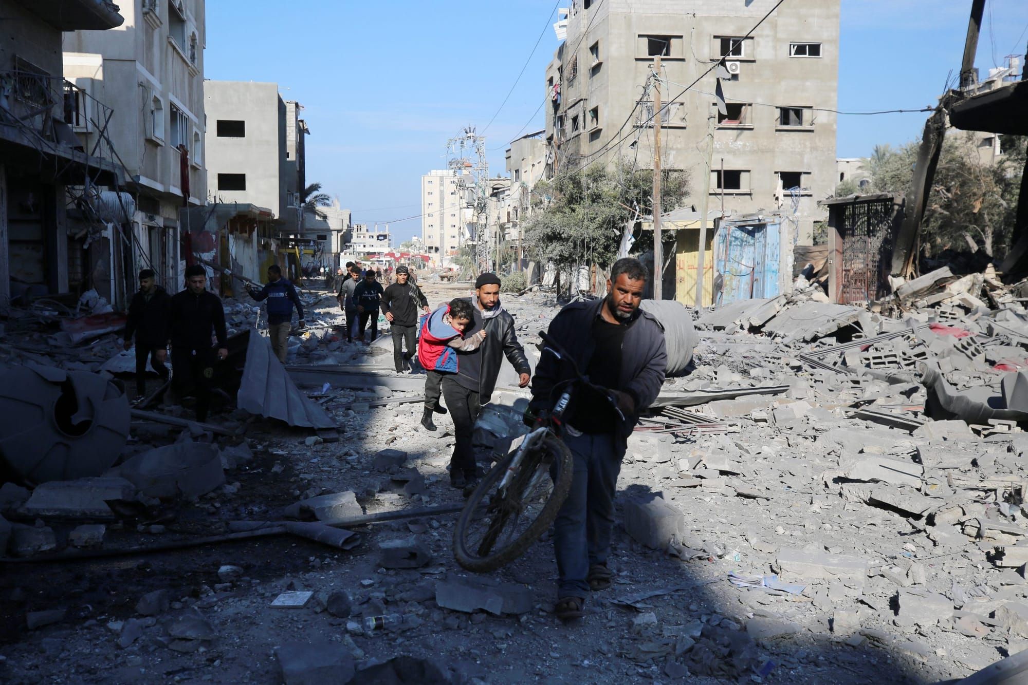 color photograph of Palestinians walking on a rubble-covered road towards the camera