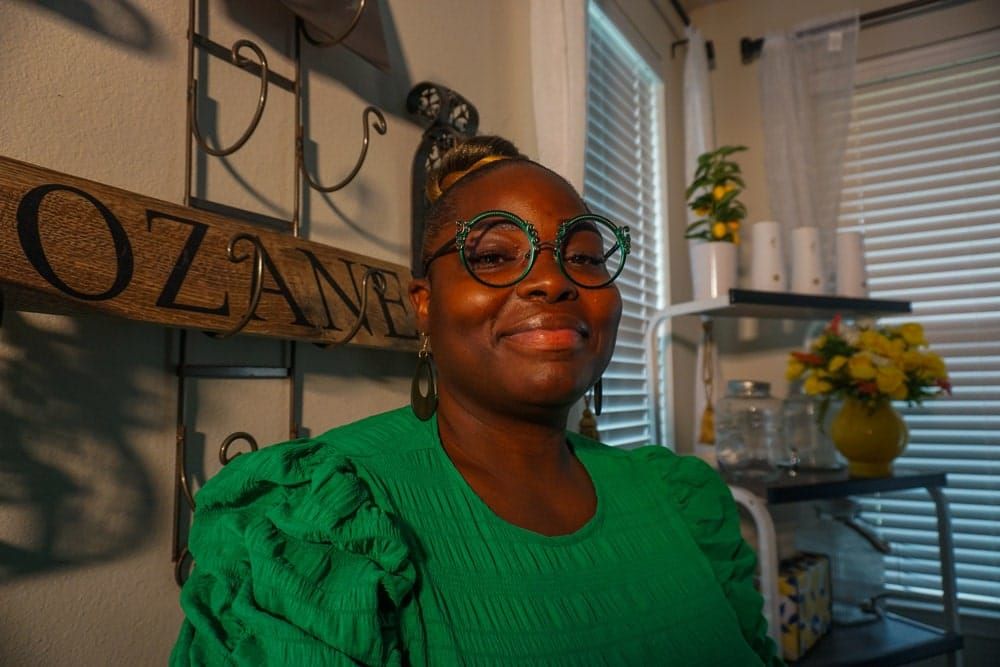 color photograph portrait of a Black woman wearing a vibrant green blouse with puffed sleeves. she sits in her house in front