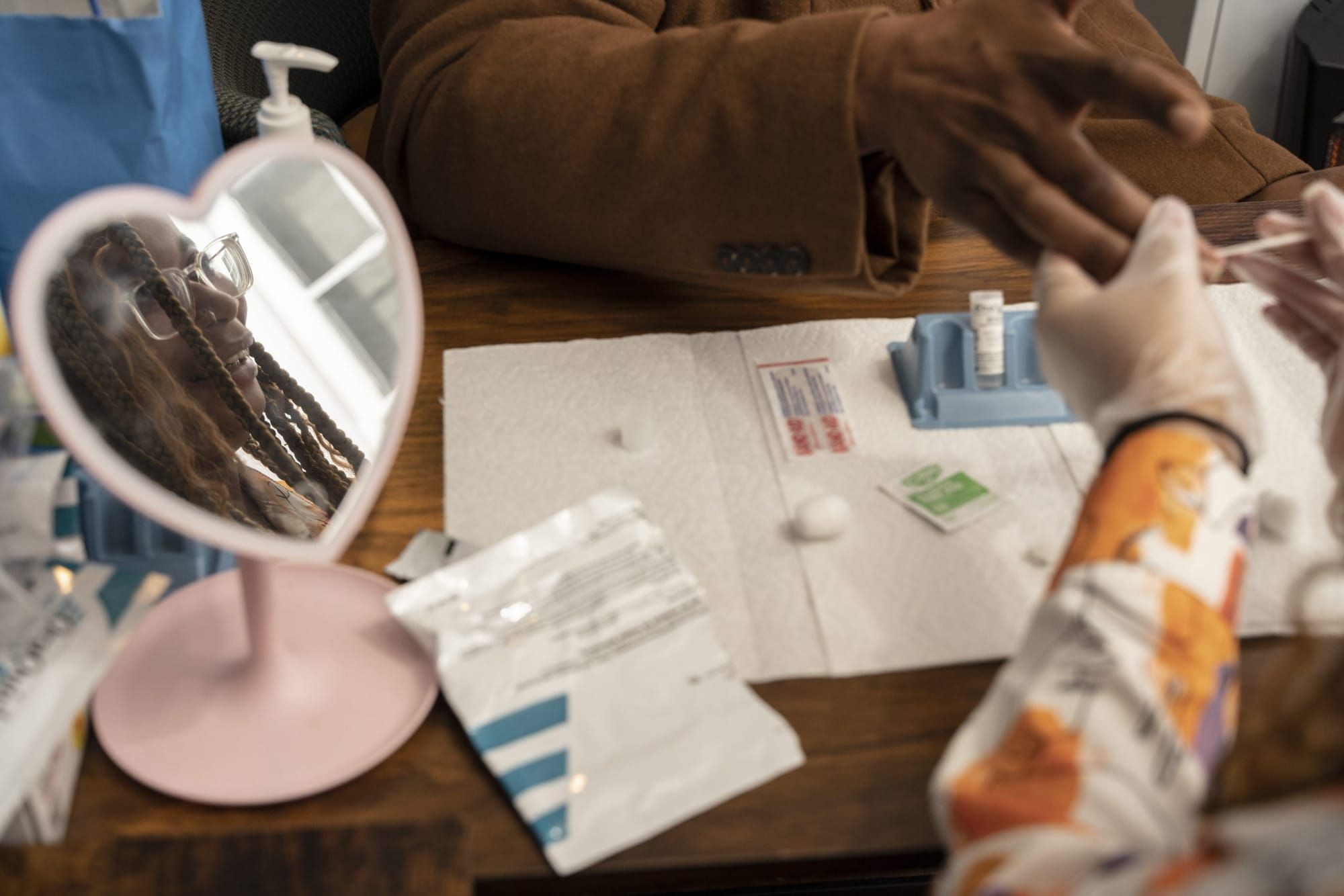 color photograph of a person getting tested for HIV. a heart-shaped mirror sits on the desk between the two people, reflectin