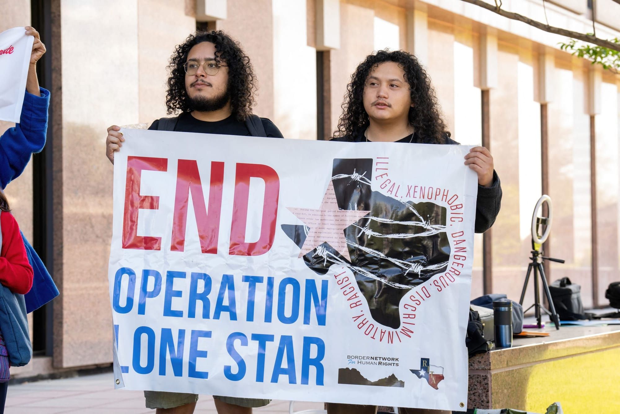 color photograph of an outdoor protest in support of immigrant rights. two people hold a large poster reading "end operation