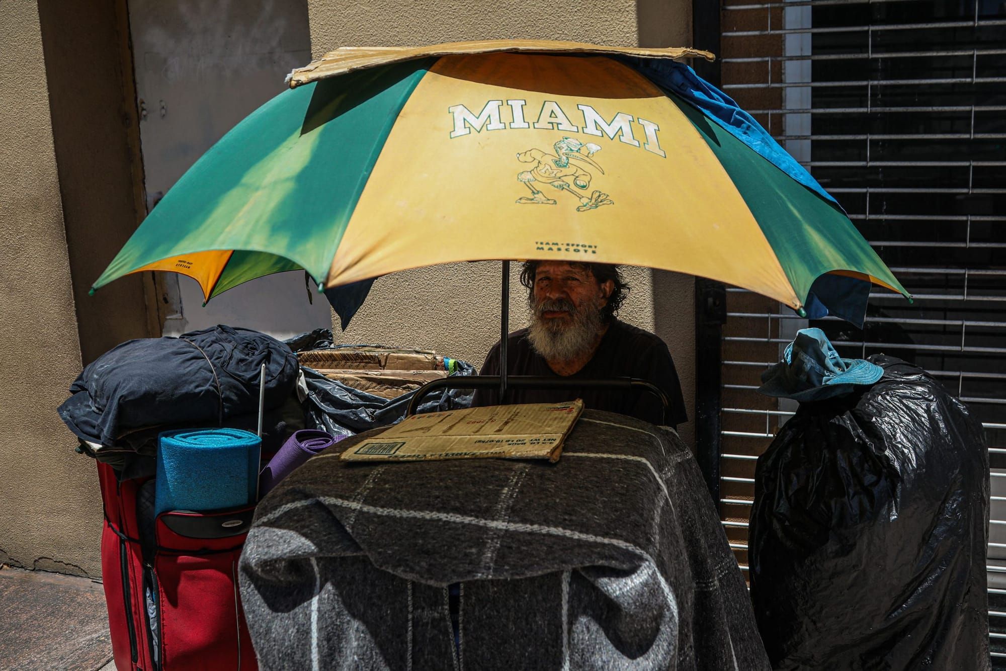 color photograph of a houseless person sitting under the shade of a large yellow and green umbrella