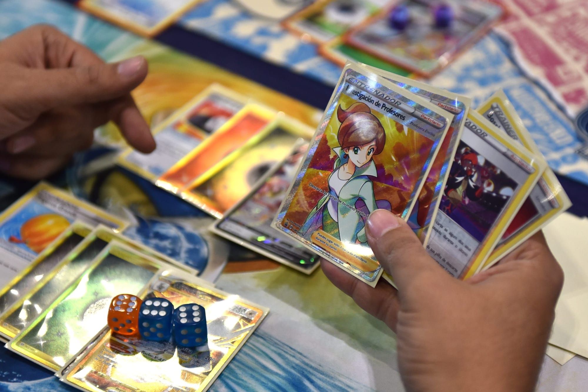 color photograph close-up of a person's hands holding pokemon cards with cards spread out on the table beneath them