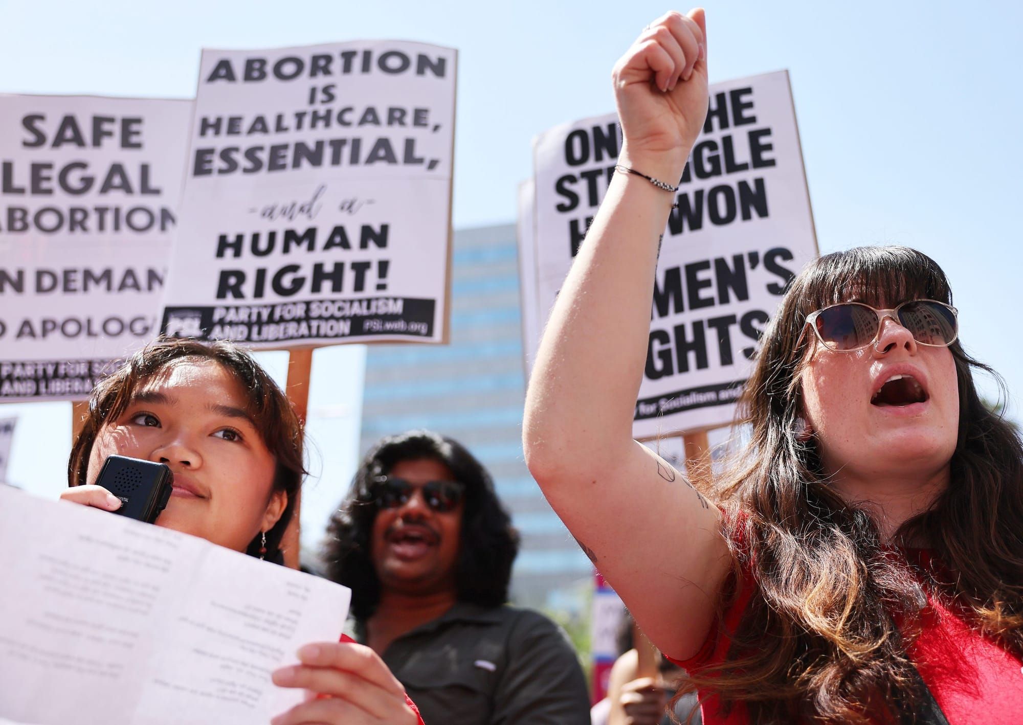 color photograph of an outdoor protest in support of abortion. people hold white picket signs with pro-abortion messages, inc