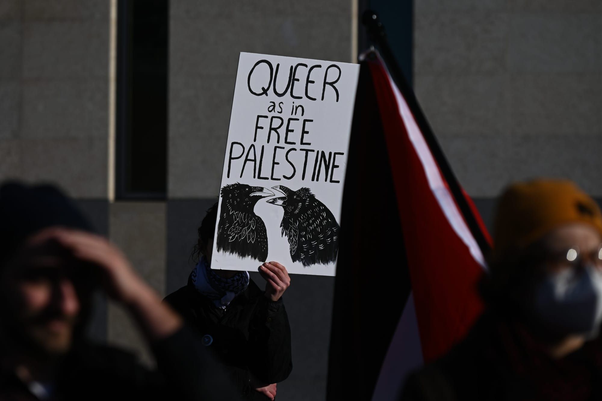 color photograph of a white poster sign at an outdoor protest. black handwritten text reads "queer as in free palestine" with