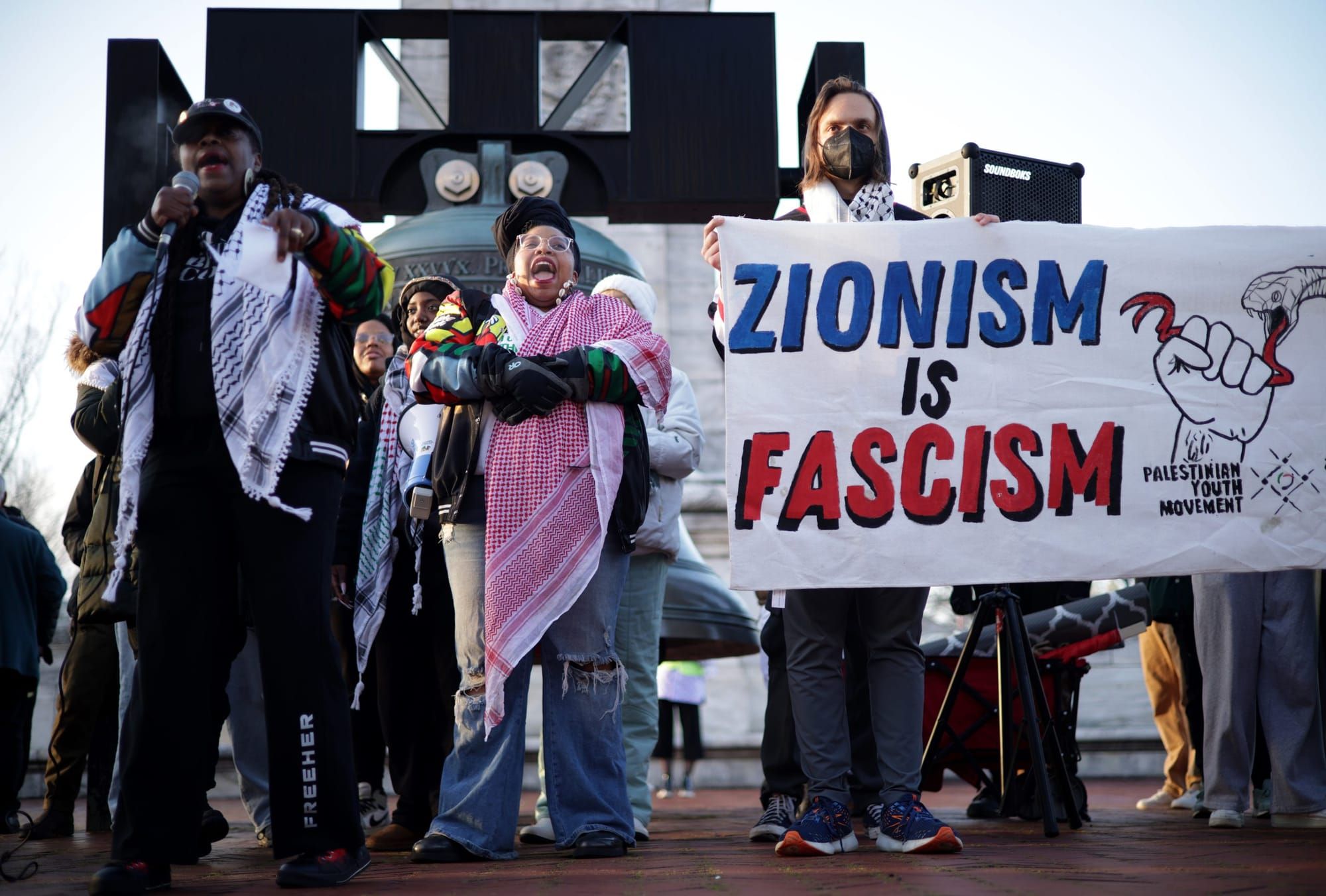 color photograph of an outdoor protest in support of palestinian liberation. in the foreground someone holds a poster reading