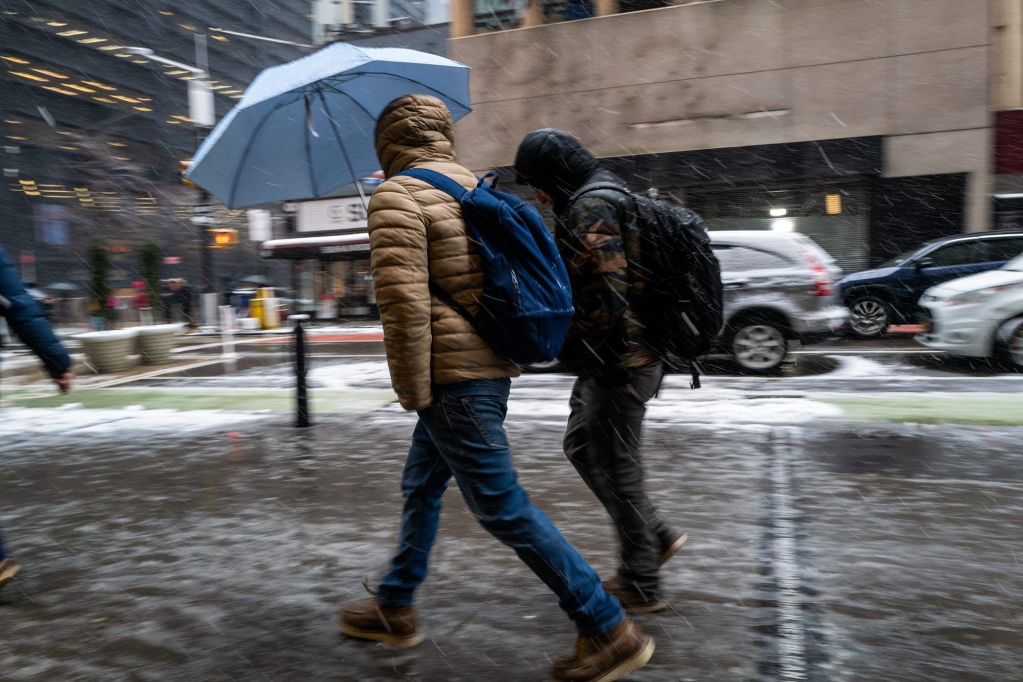 color photograph of two students walking in a snowstorm along an urban sidewalk