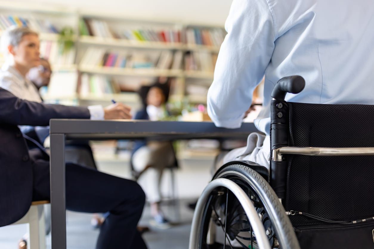 color stock photograph of a person in a wheelchair sitting at a work conference table in a bright room