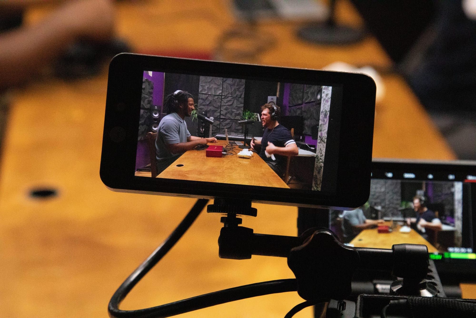 color photograph of a video camera display lens showing two people sitting at a wooden table recording a podcast