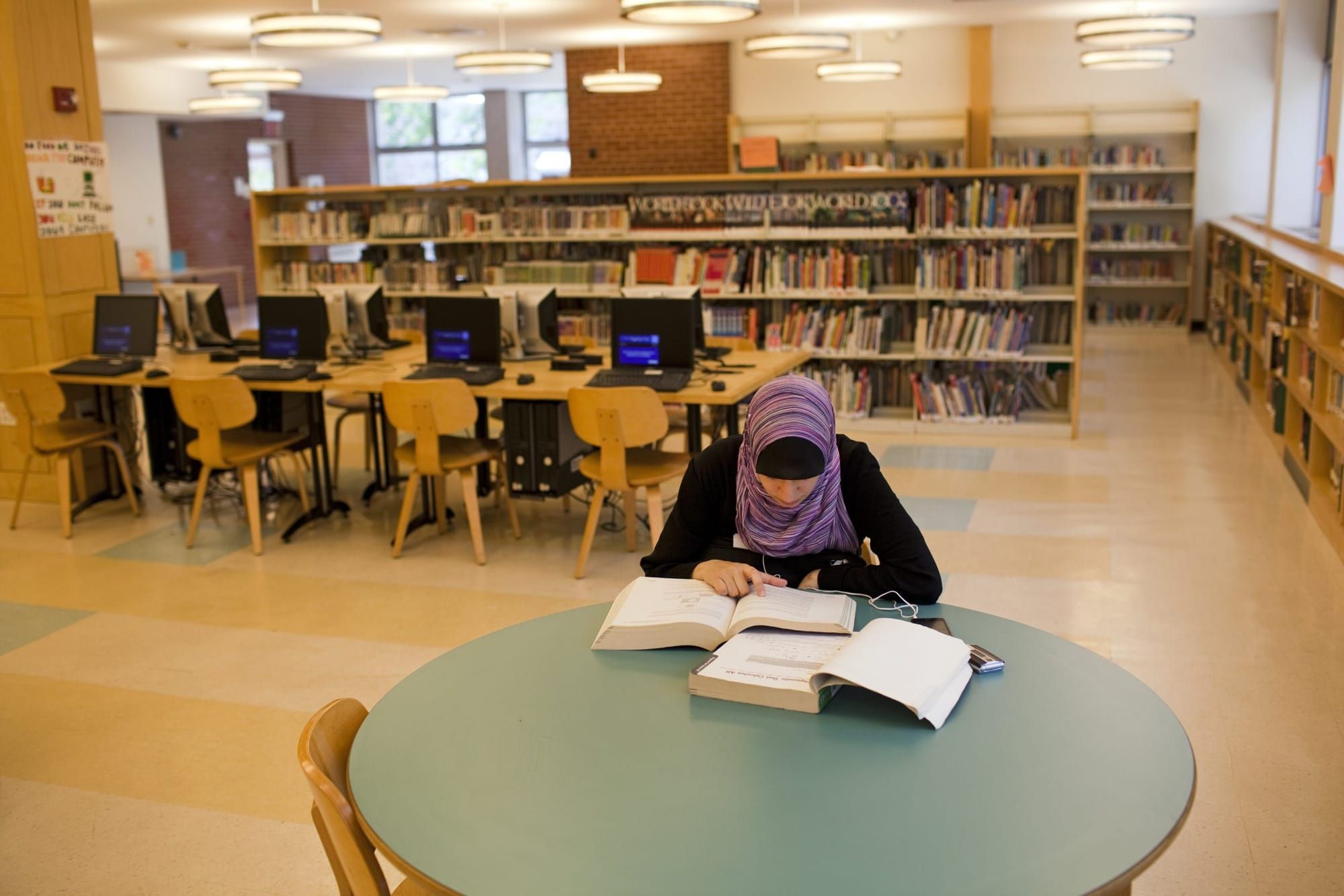 color photograph of a young woman in a hijab studying in a public library