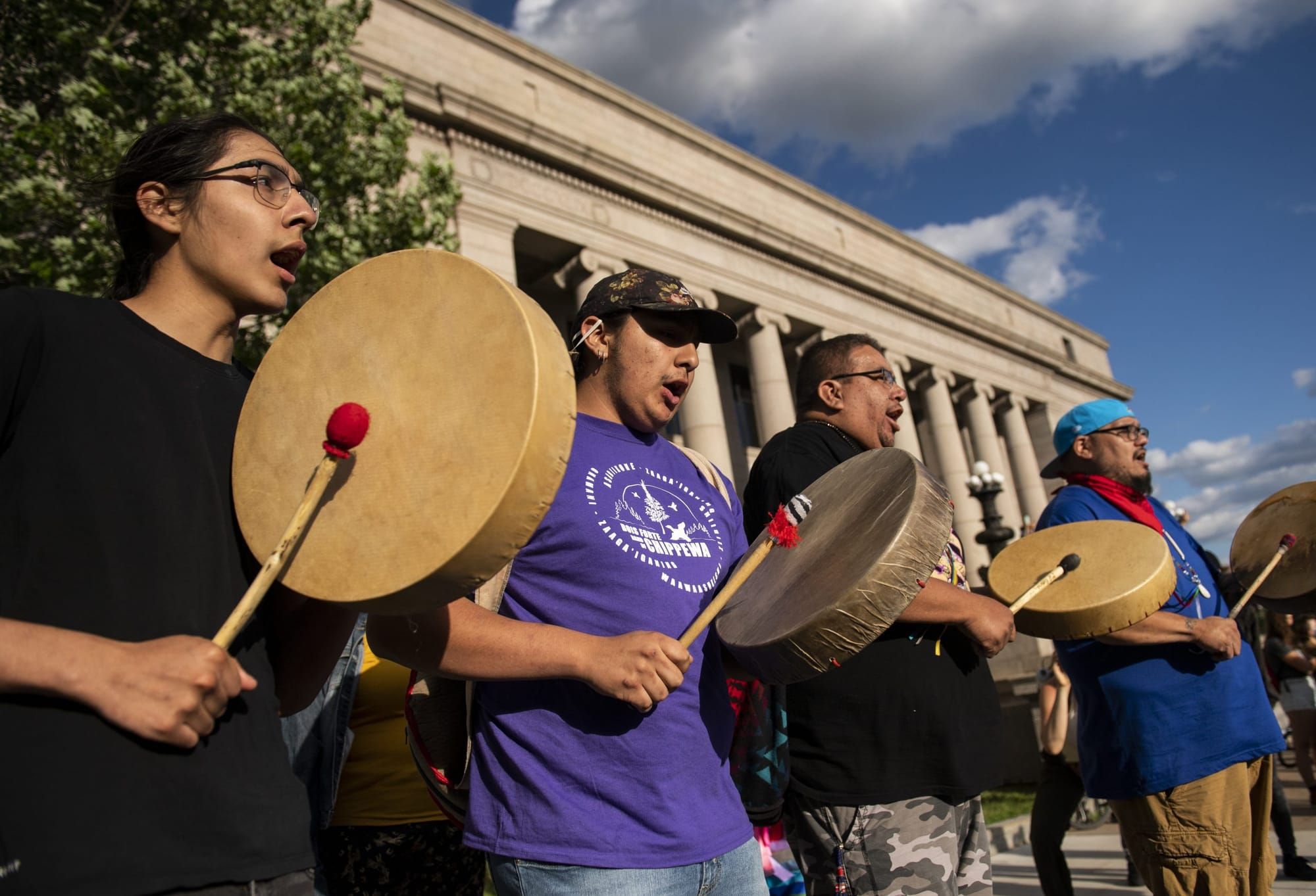 color photograph of an outdoor protest. indigenous people beat drums outside the Minnesota state capitol building