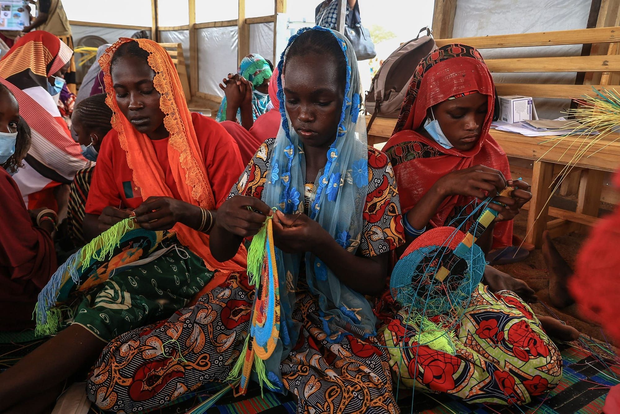 color photograph of three Black women wearing brightly colored head coverings making fans