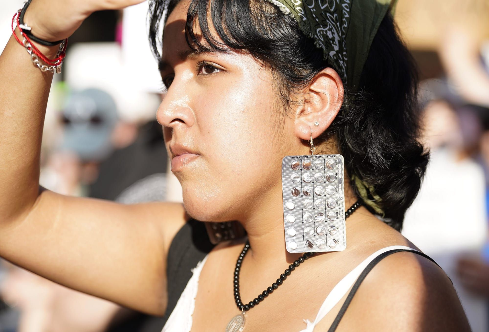 color photograph of a young woman wearing hand-made earrings made of birth control pills