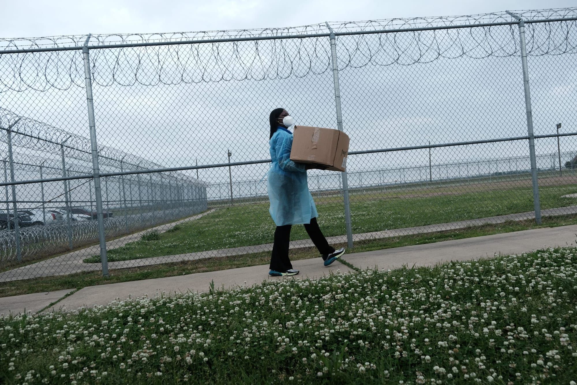 color photograph of a person wearing personal protective equipment carrying a cardboard box while walking along a barbed wire