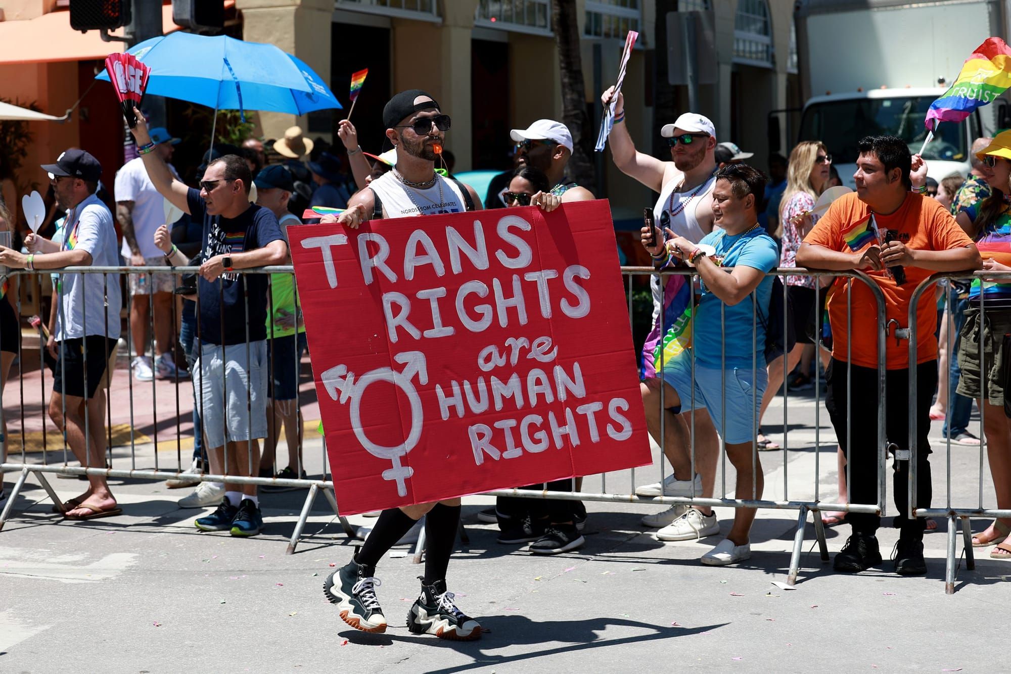 color photograph of a queer Pride celebration. a person in the mid-ground holds a red sign that reads "Trans rights are human