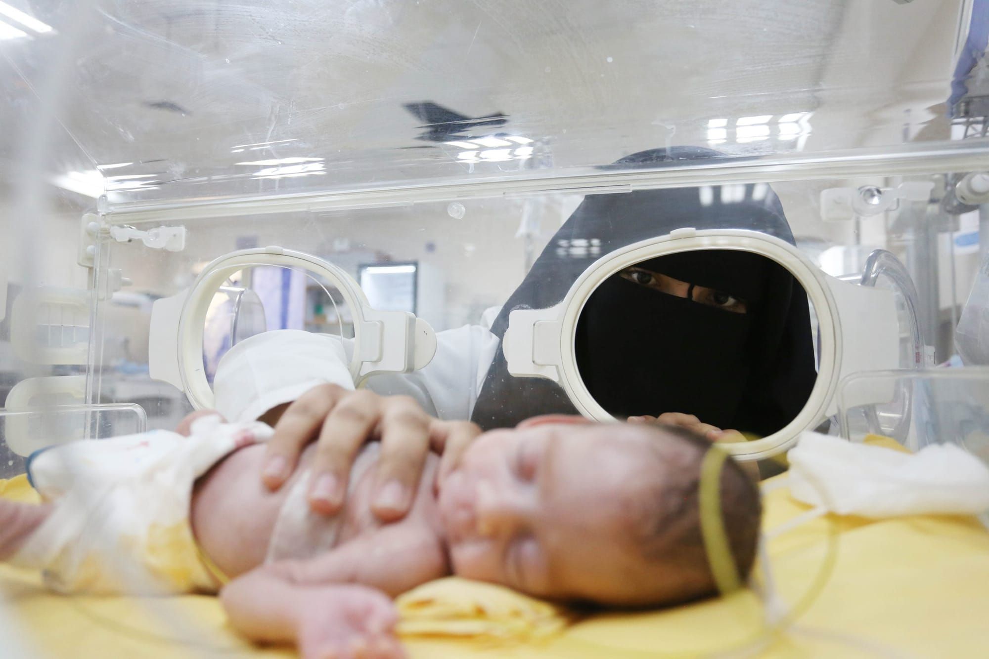 color photograph of a female doctor wearing a face and body covering checking on a preterm baby in a ventilator