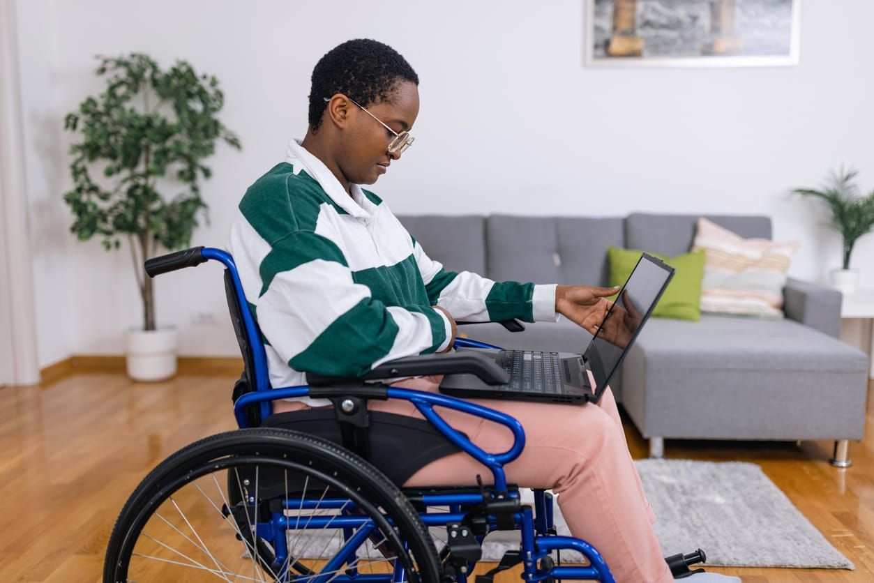 color stock photo of a Black person wearing a green and white rugby shirt sitting in a wheelchair on their laptop