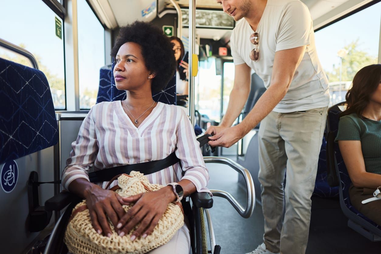 color stock photo of a Black woman wearing a striped long-sleeve shirt. she sits in a wheelchair on a public transit bus