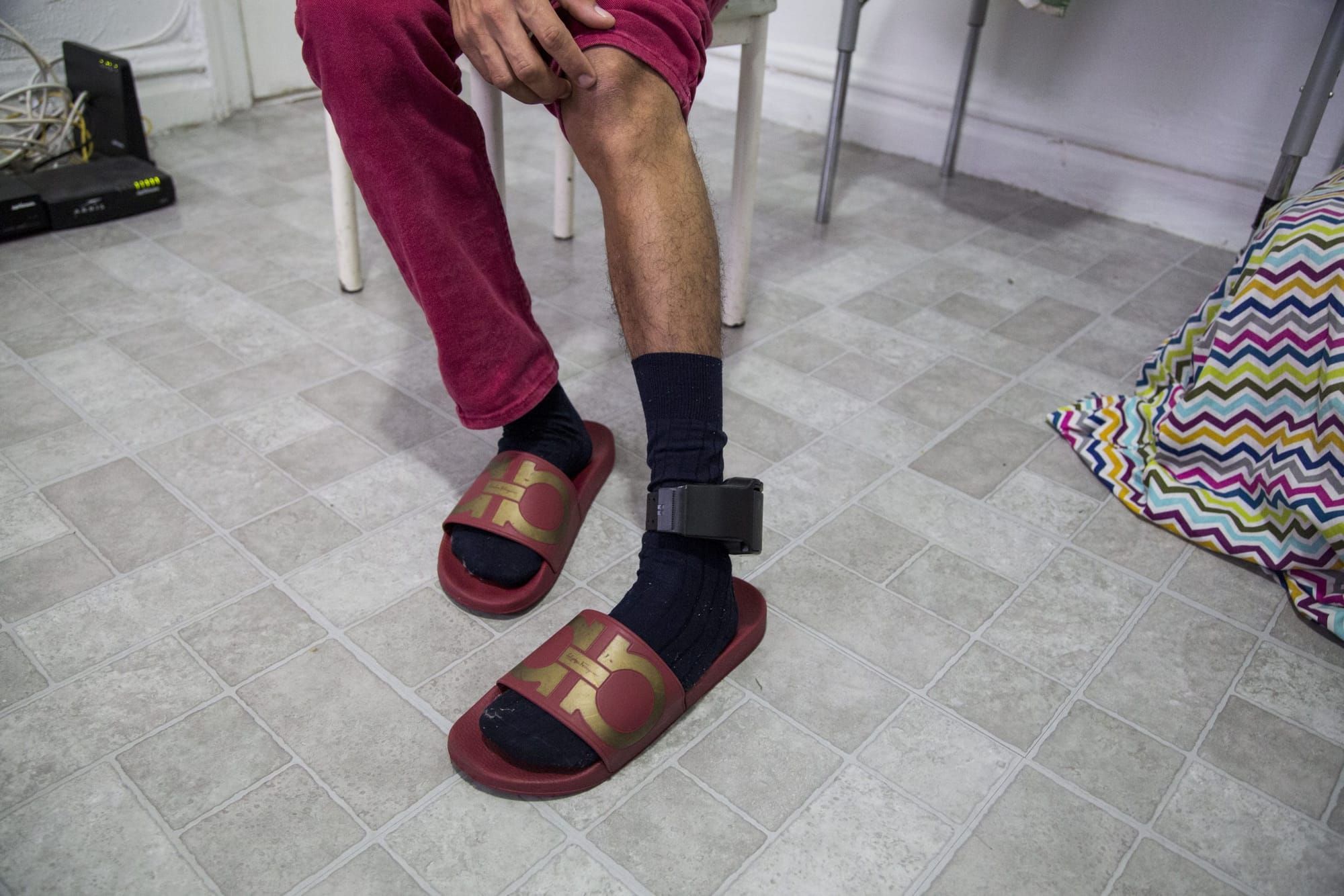 color photograph of a person pulling their pant leg up to reveal a black ankle monitor