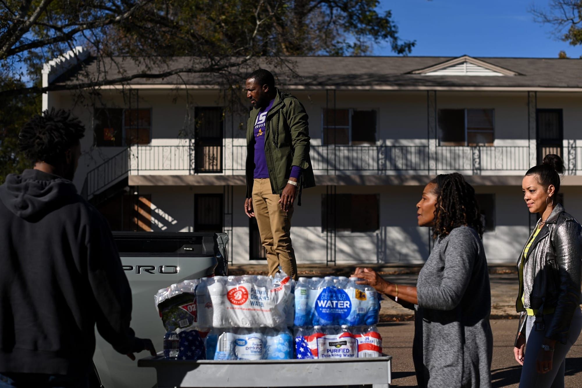 color photograph of a Black man standing on a pack of water bottles in front of a church