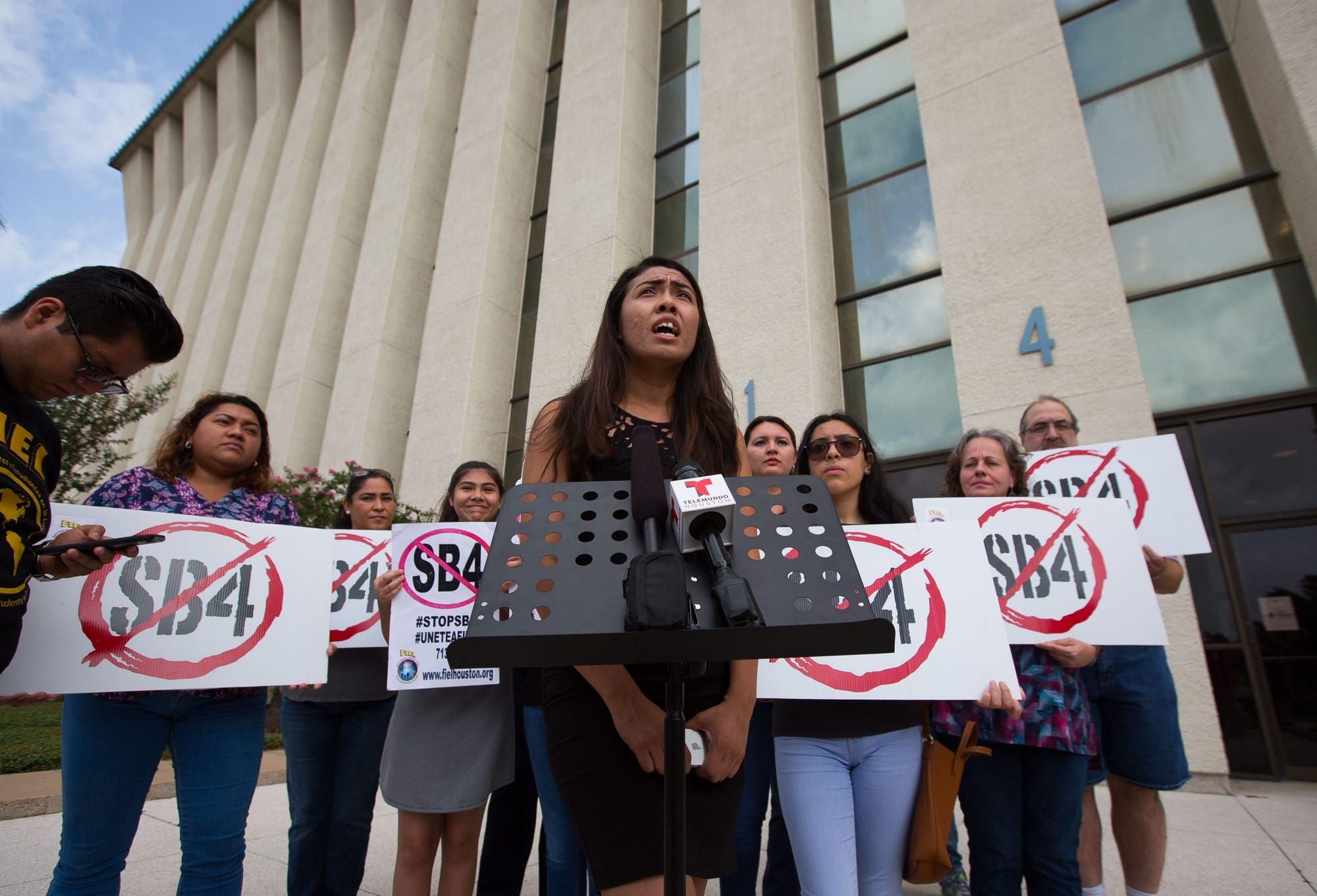 color photograph of an outdoor protest where people hold up signs with red negative circles over the text "SB 4"
