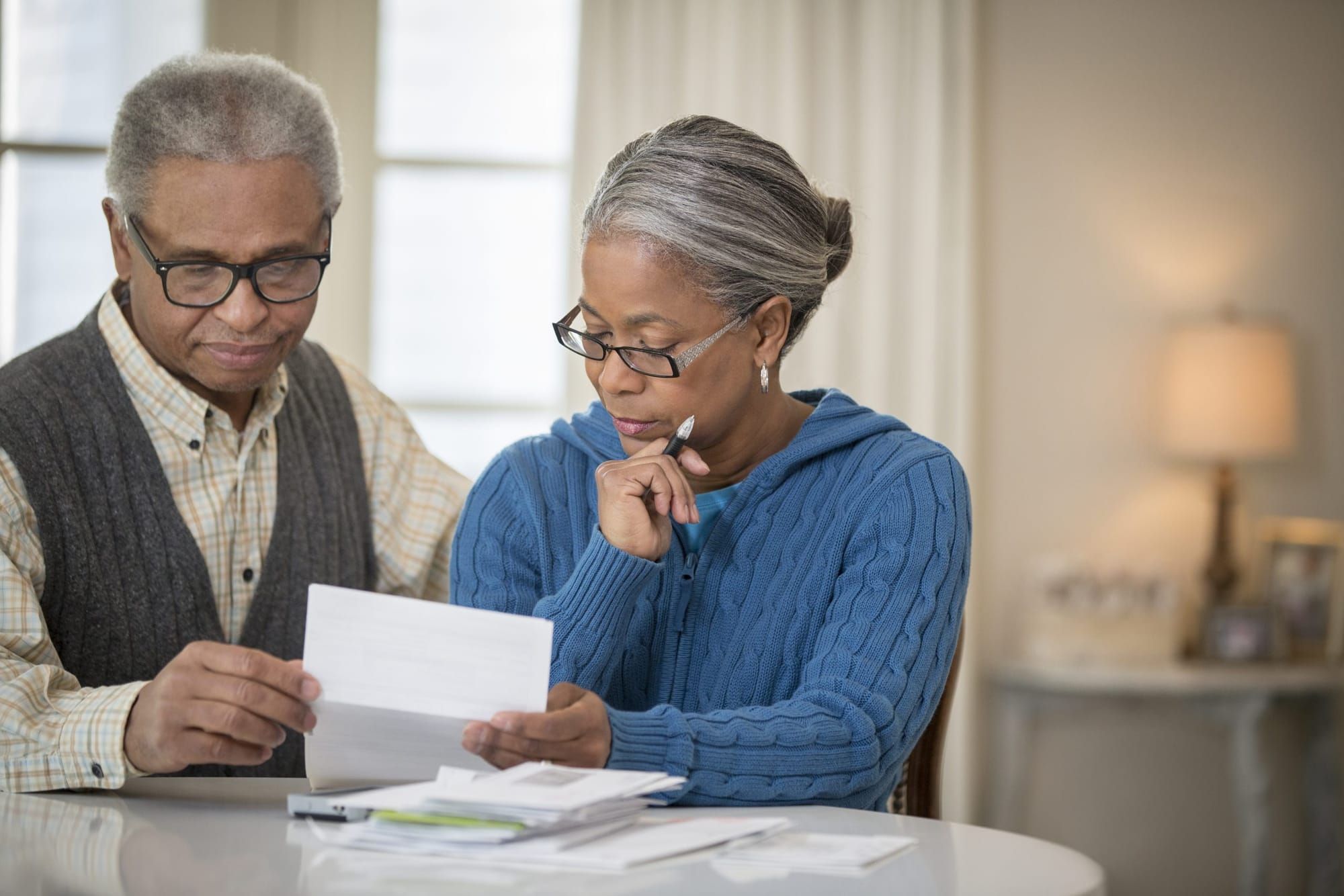 color stock photo of an older Black couple sitting at a table in their house looking at a bill