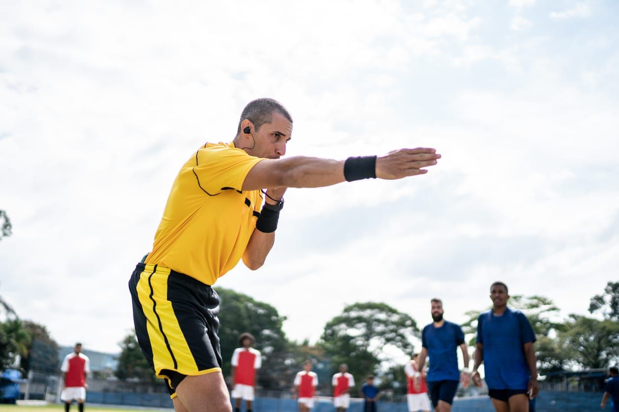 color stock photo of a referee in a yellow shirt blowing his whistle and gesturing towards the field during a soccer match