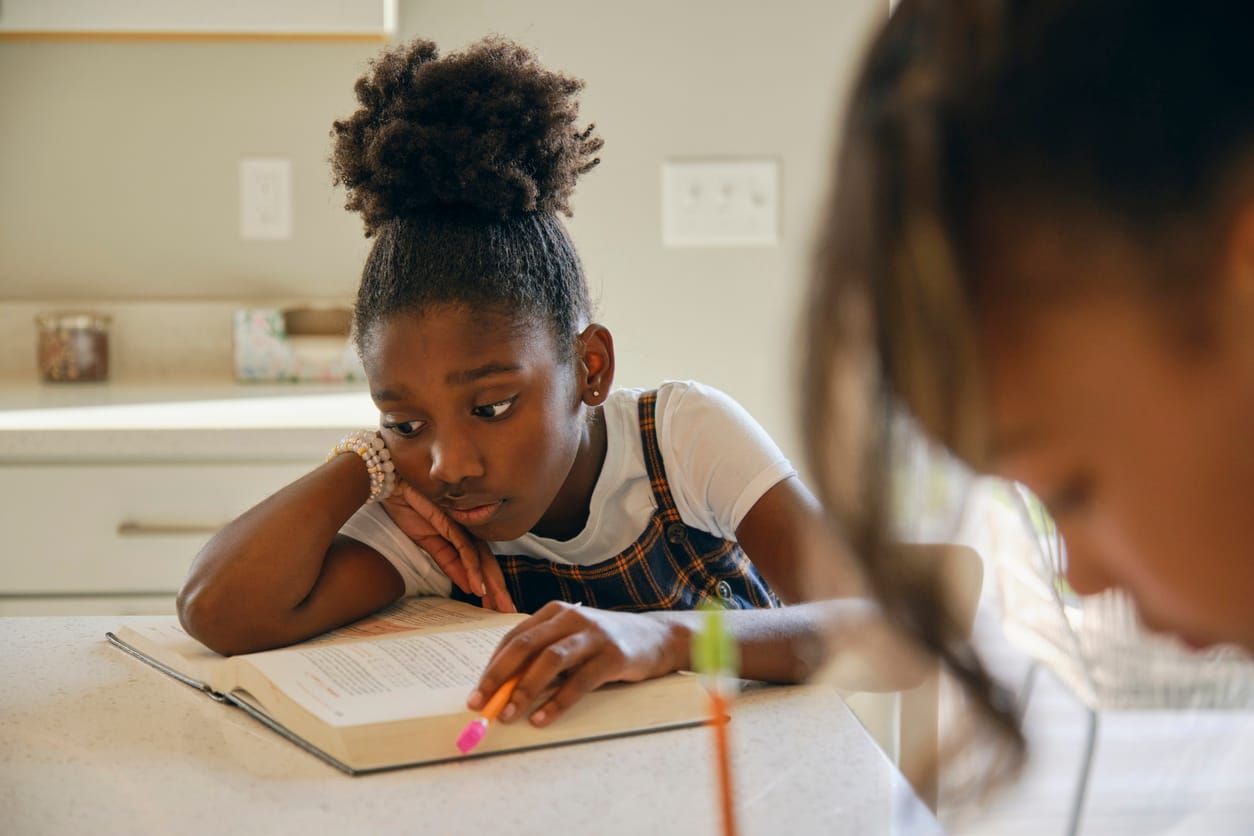 color stock photo of a young dark-skinned Black girl with natural hair pulled back in a ponytail. she sits at a table leaning