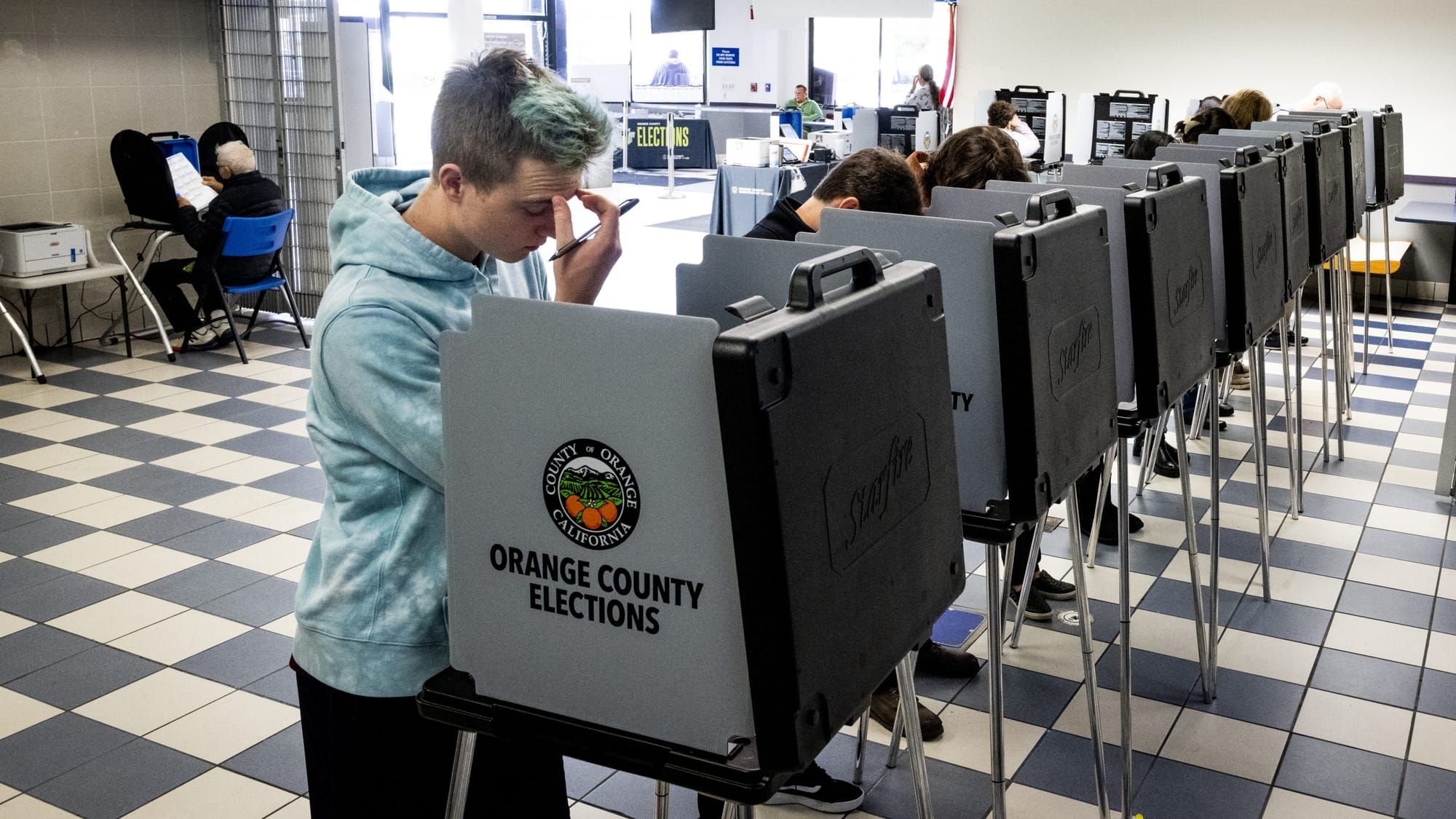 color photograph of a young person with short blue hair looking frustrated at a voting booth
