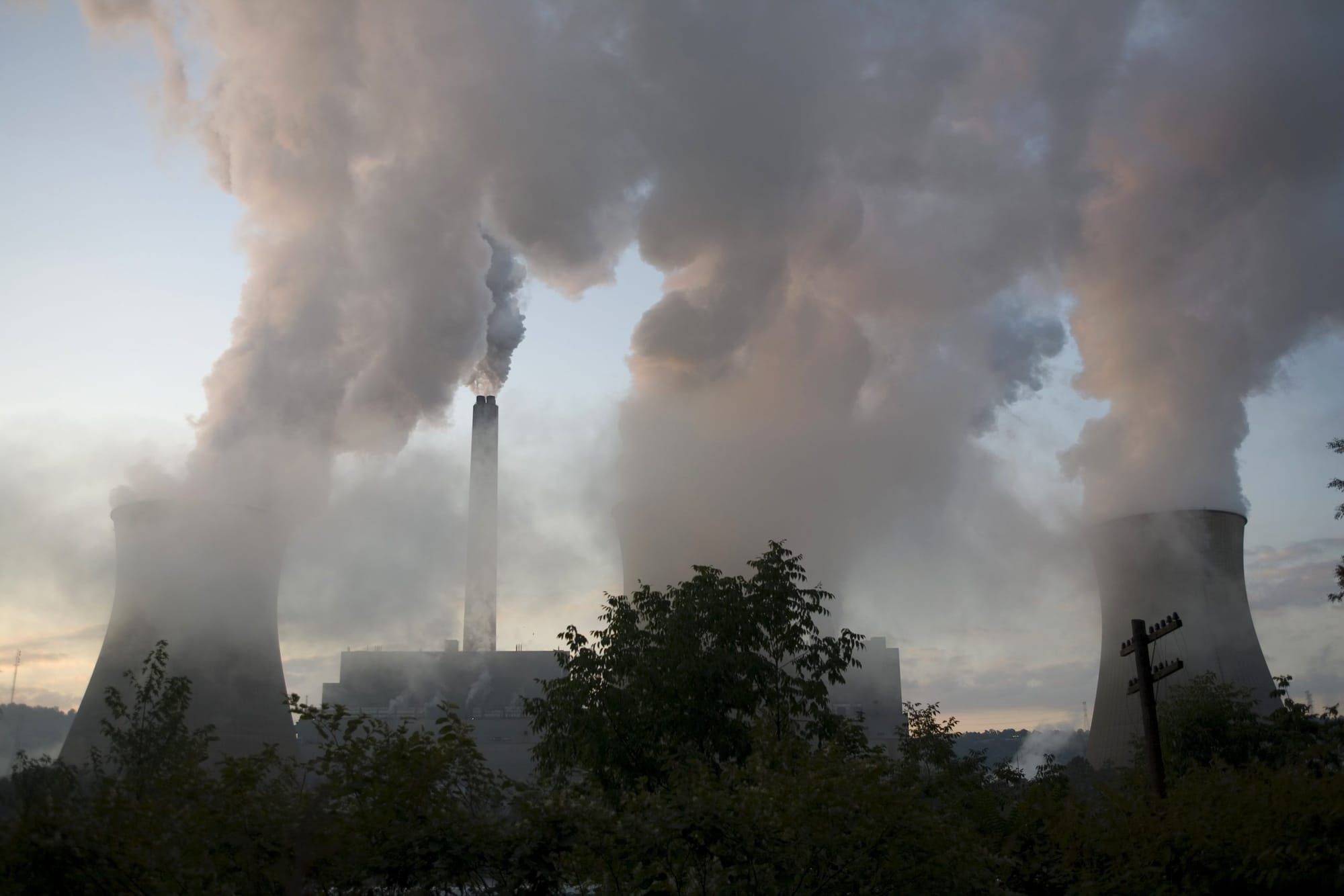 color photograph of three power plant smoke stacks belching smoke into the air. smog hangs low to the ground in the foregroun