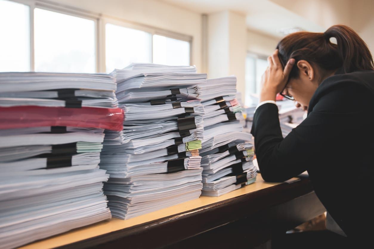 color photograph of a stressed lawyer sitting at a desk with several piles of paperwork beside her