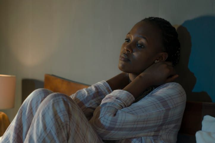color photograph of a young Black girl wearing pajamas sitting in bed looking anxious