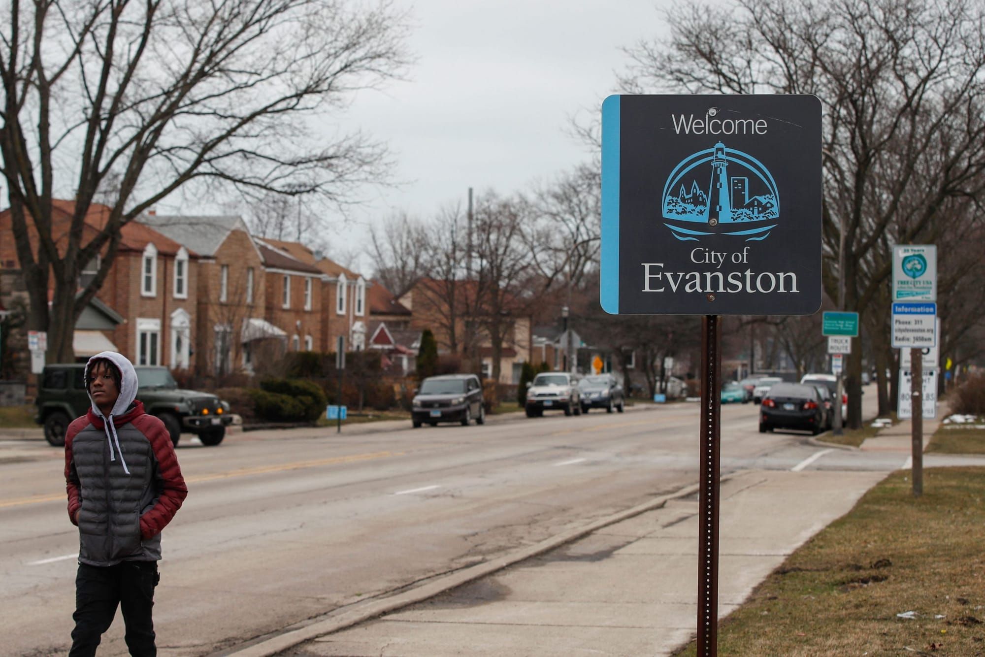 color photograph of a Black man walking along a sidewalk past a sign that reads "Welcome to Evanston"