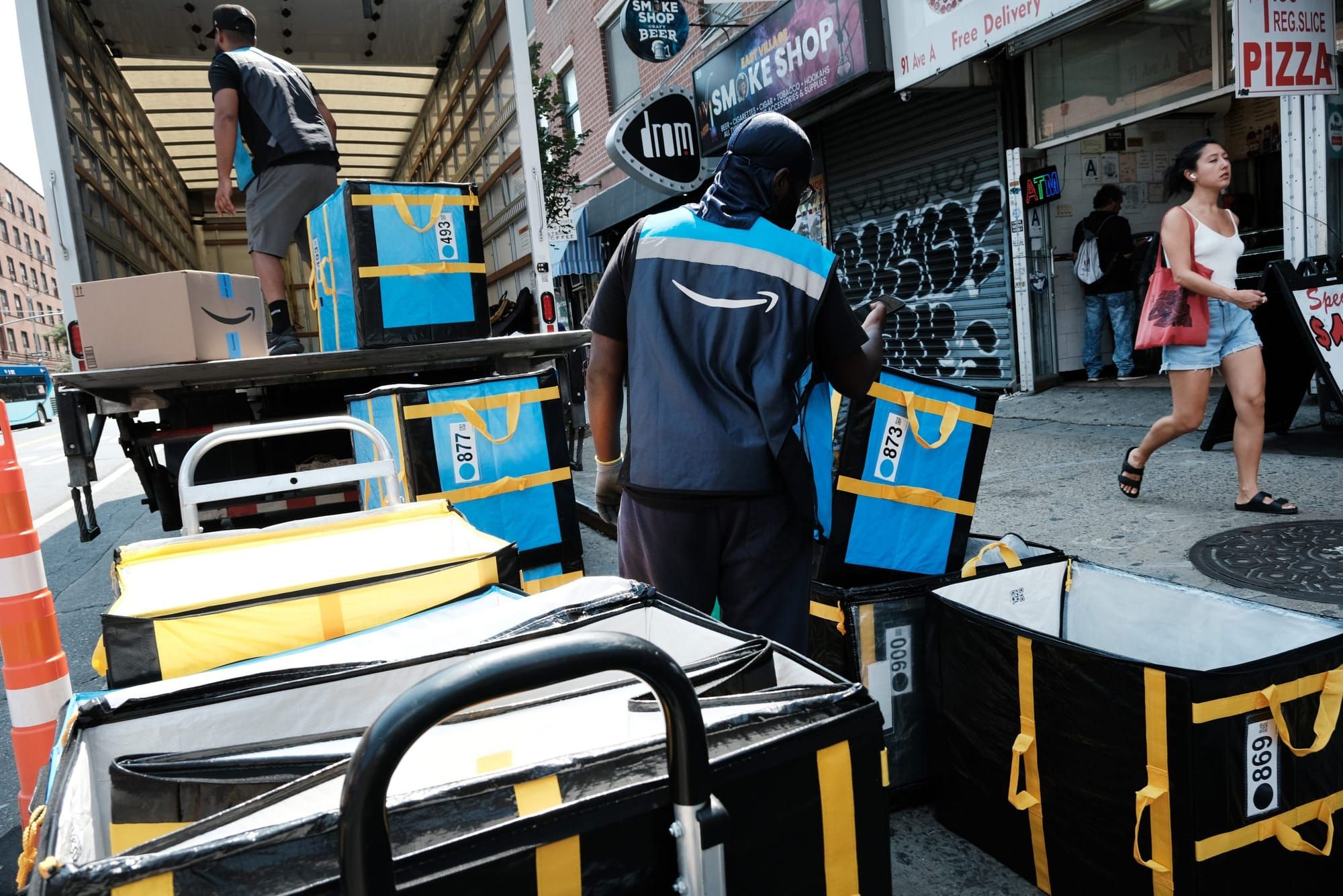 color photograph of an Amazon worker in a blue vest with the Amazon curved arrow on the back unloading a truck full of packag