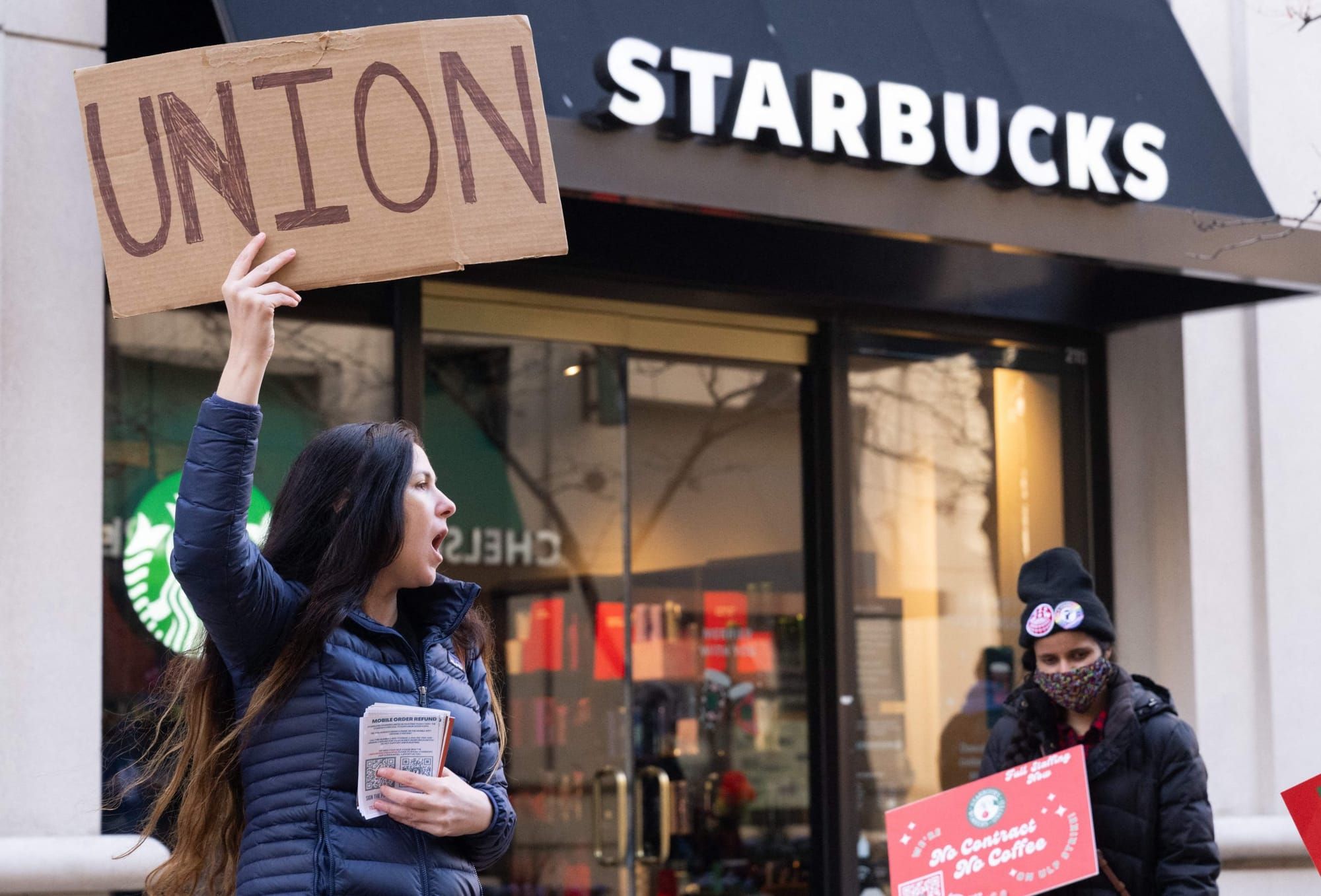 color photograph of a pro-union protest outside of a Starbucks store. a person with long black hair wearing a black coat hold