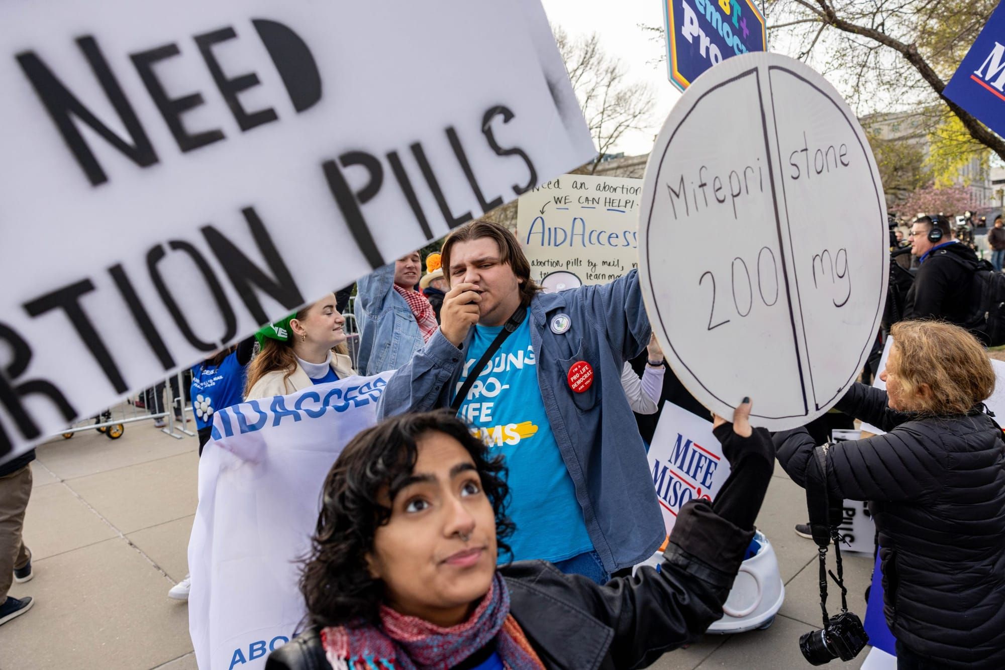 color photograph of an outdoor protest in support of abortion access. to the left, someone holds a sign reading "need abortio