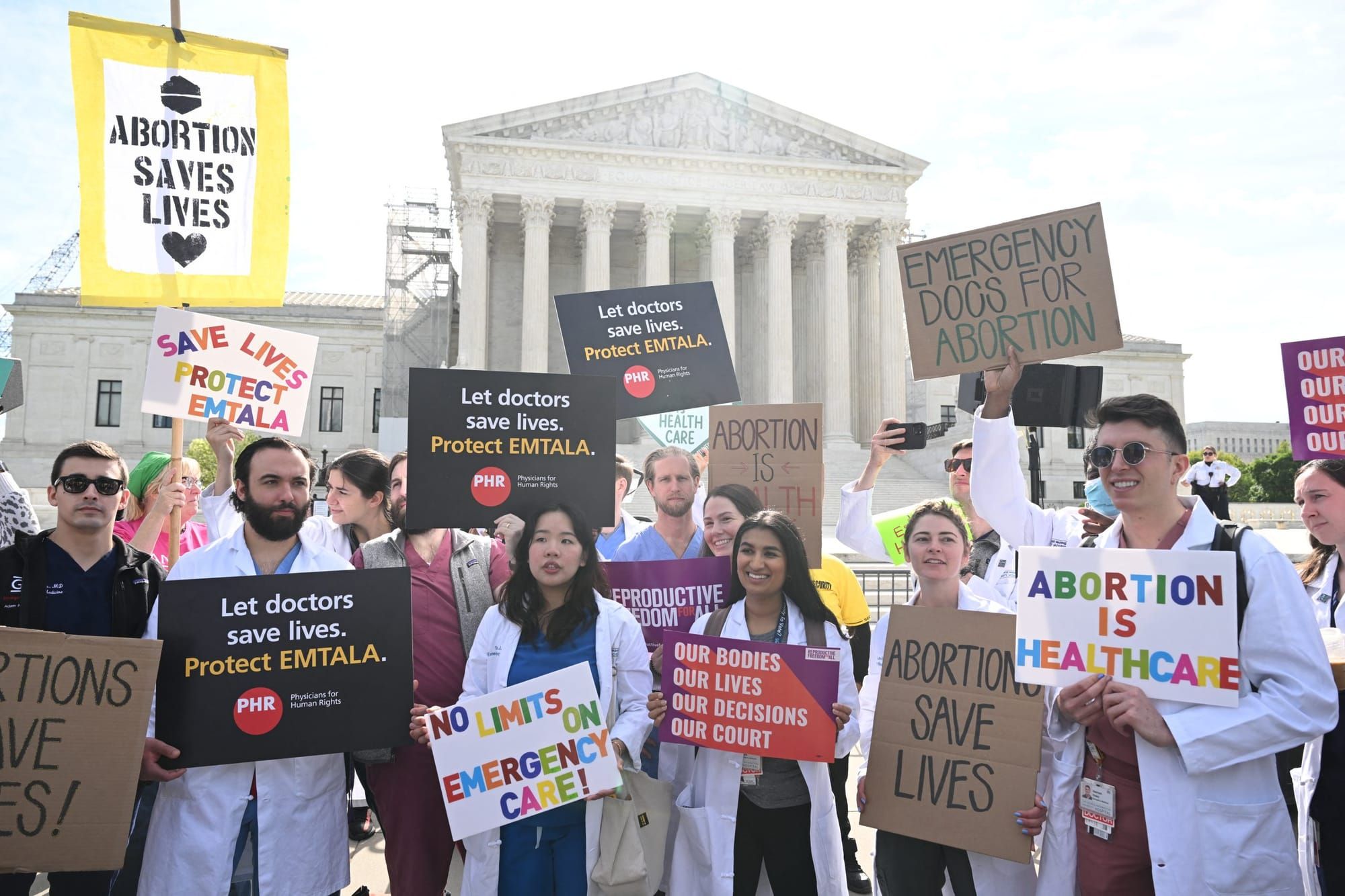 color photograph of a protest outside the Supreme Court building. medical workers carry signs in support of EMTALA and aborti
