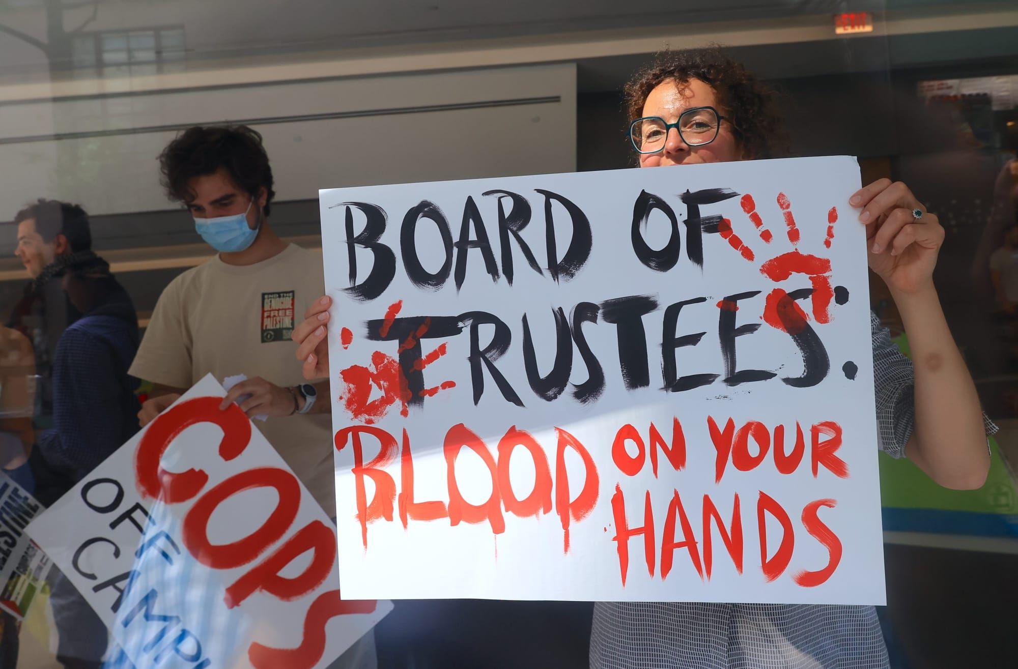color photograph of a person holding up a poster at a pro-Palestine protest. the poster reads "board of trustees: blood on yo