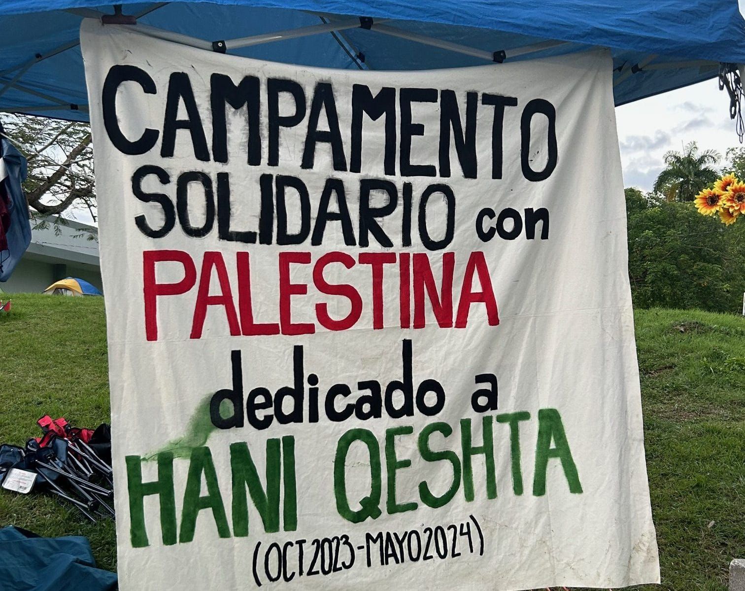 color photograph of a cloth banner that reads "campamento solidario con palestina dedicado a hani queshta"