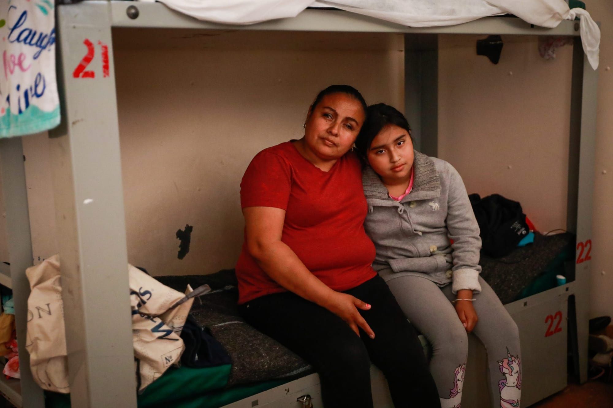 color photograph of a Latina mother and daughter sitting on a metal bunk bed in a shelter