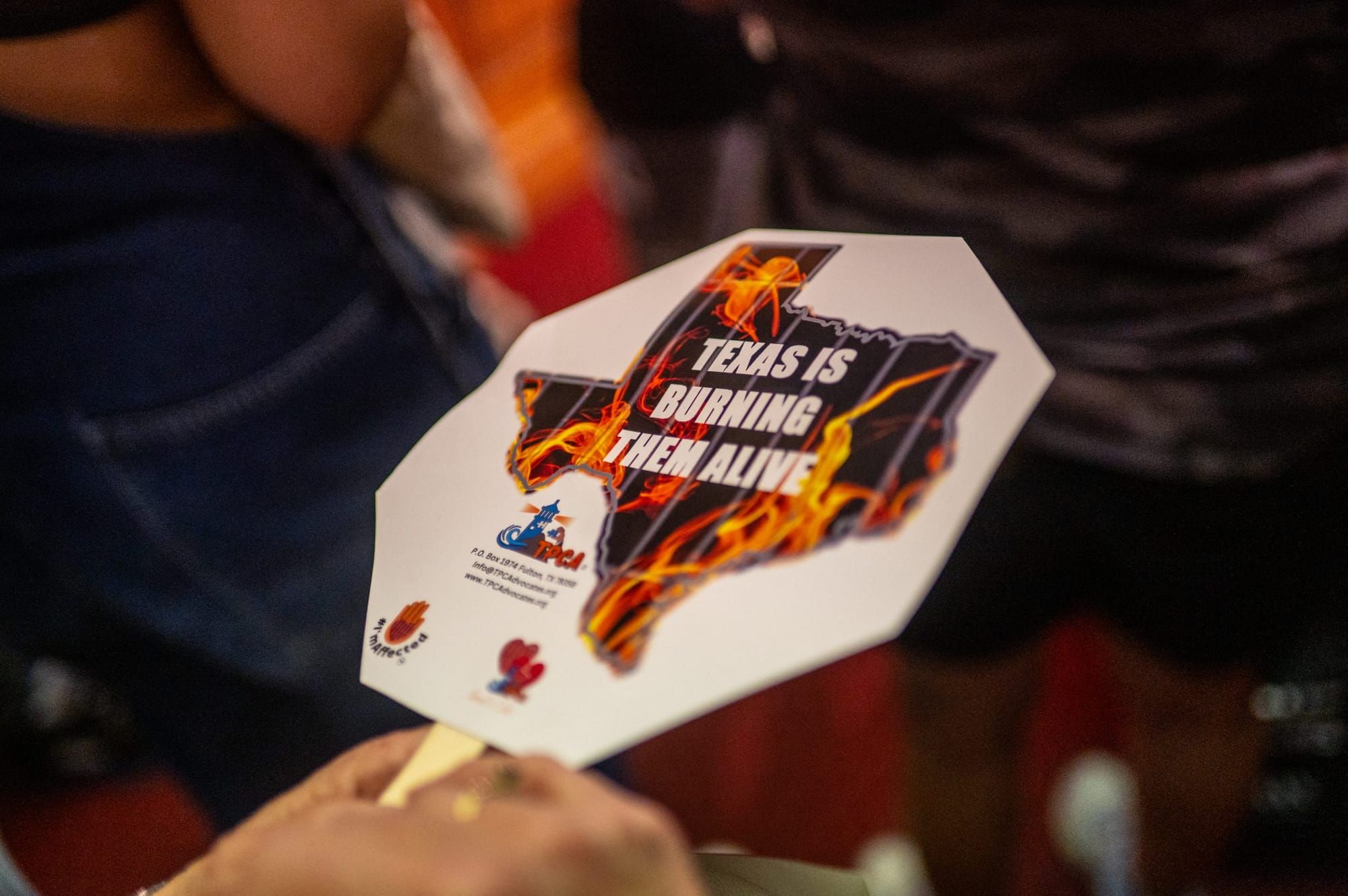 color photograph of a small handheld sign with the outline of the state of texas and the text "texas is burning them alive"