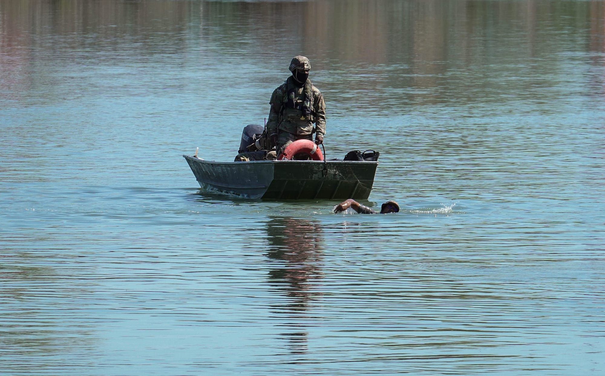 color photograph of a law enforcement officer standing on a small boat watching a person swim across the Rio Grande