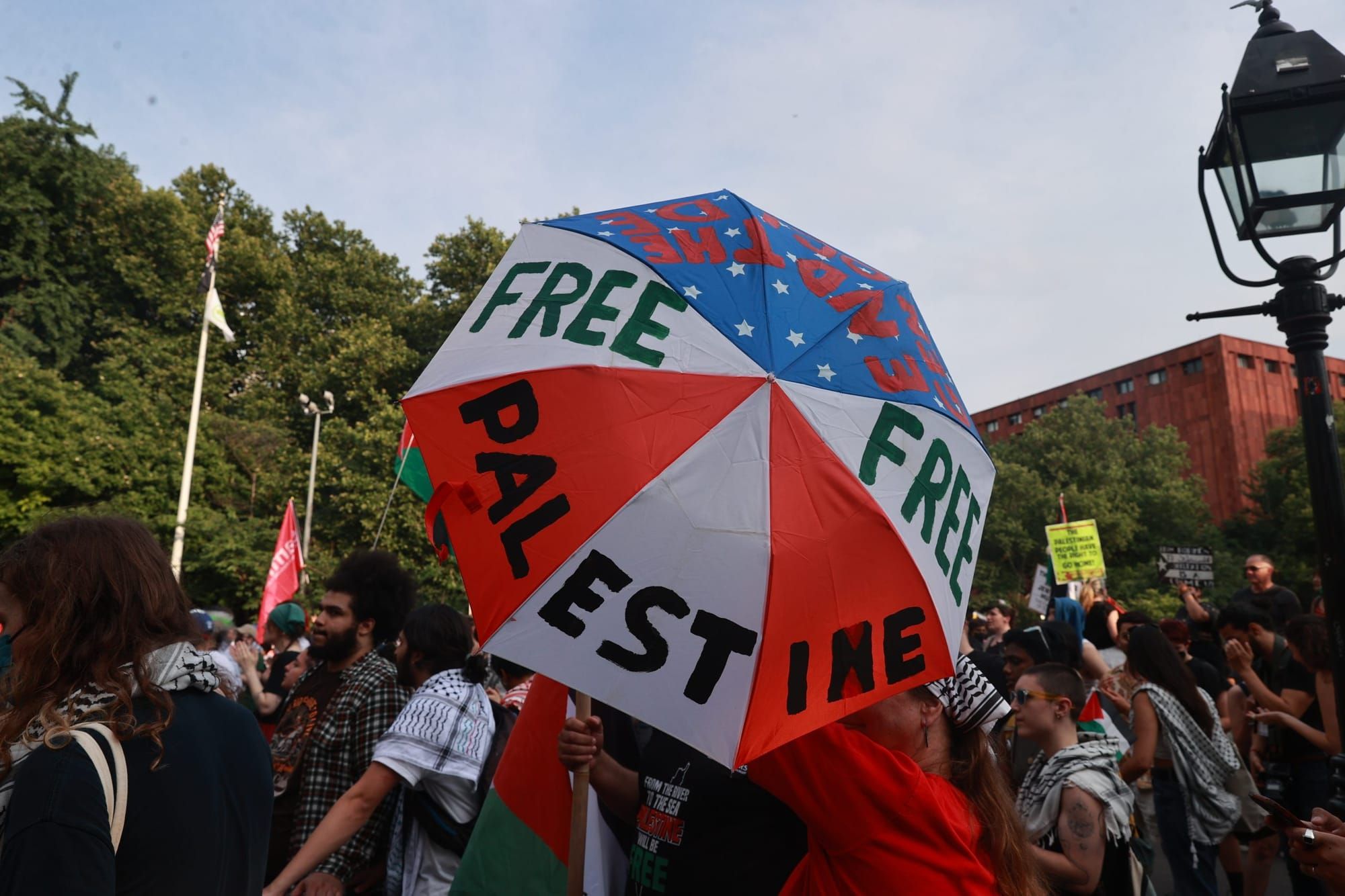 color photograph of a pro-Palestine protest. a person holds up an umbrella that conceals their face. the umbrella reads "Free