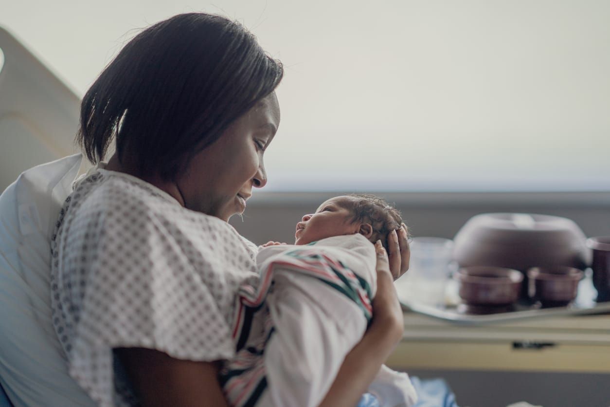 color photograph of a Black mother in a hospital gown holding a newborn infant