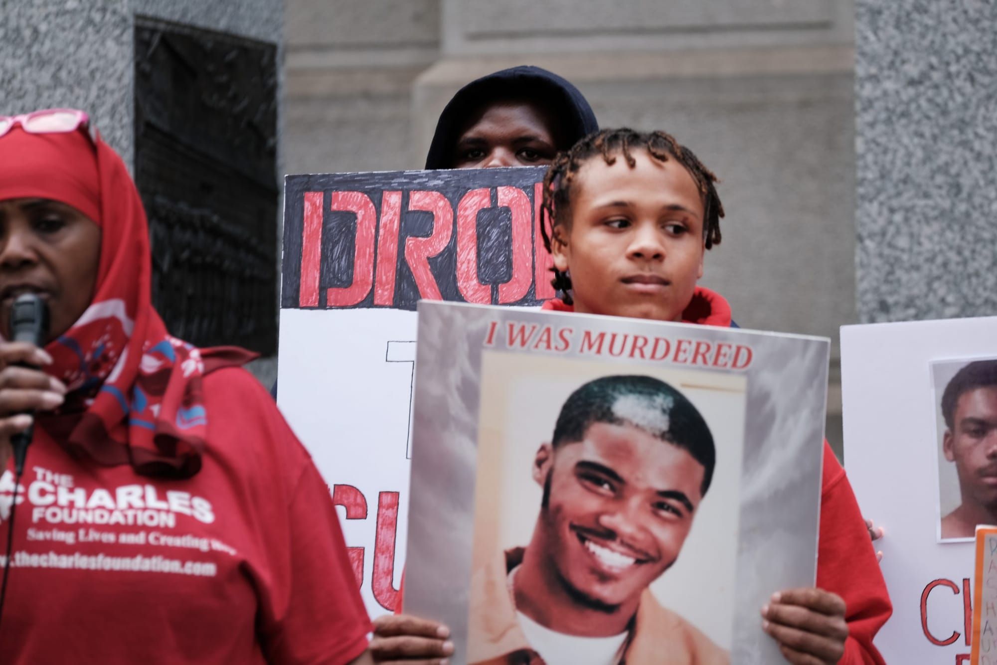 color photograph of an outdoor rally. people wear red and hold up signs with photographs of people killed by gun violence