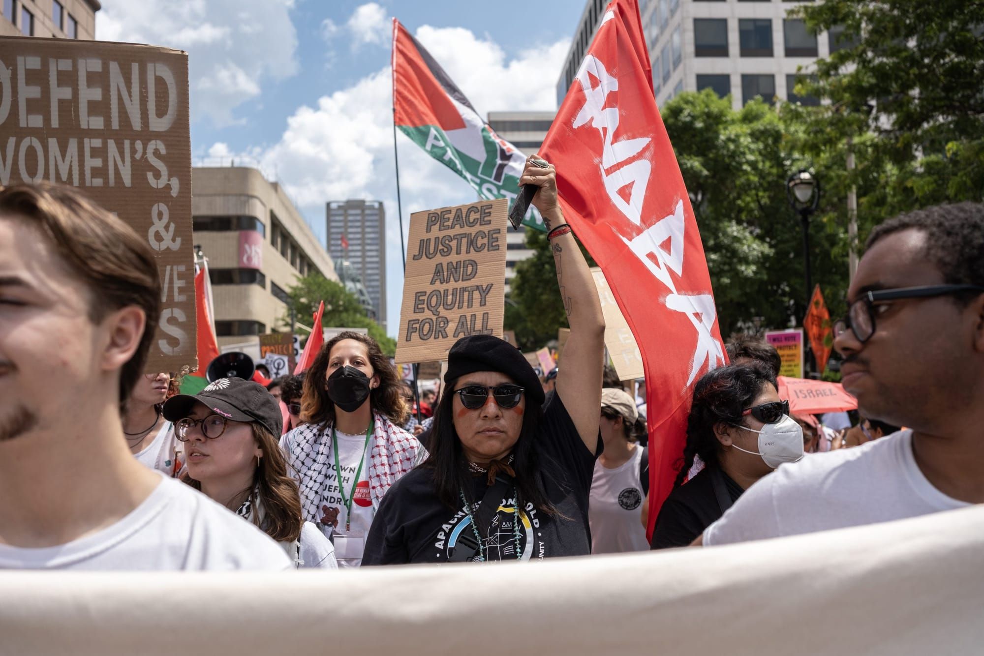 color photograph of an outdoor protest. people wave "LANDBACK" and Palestinian flags