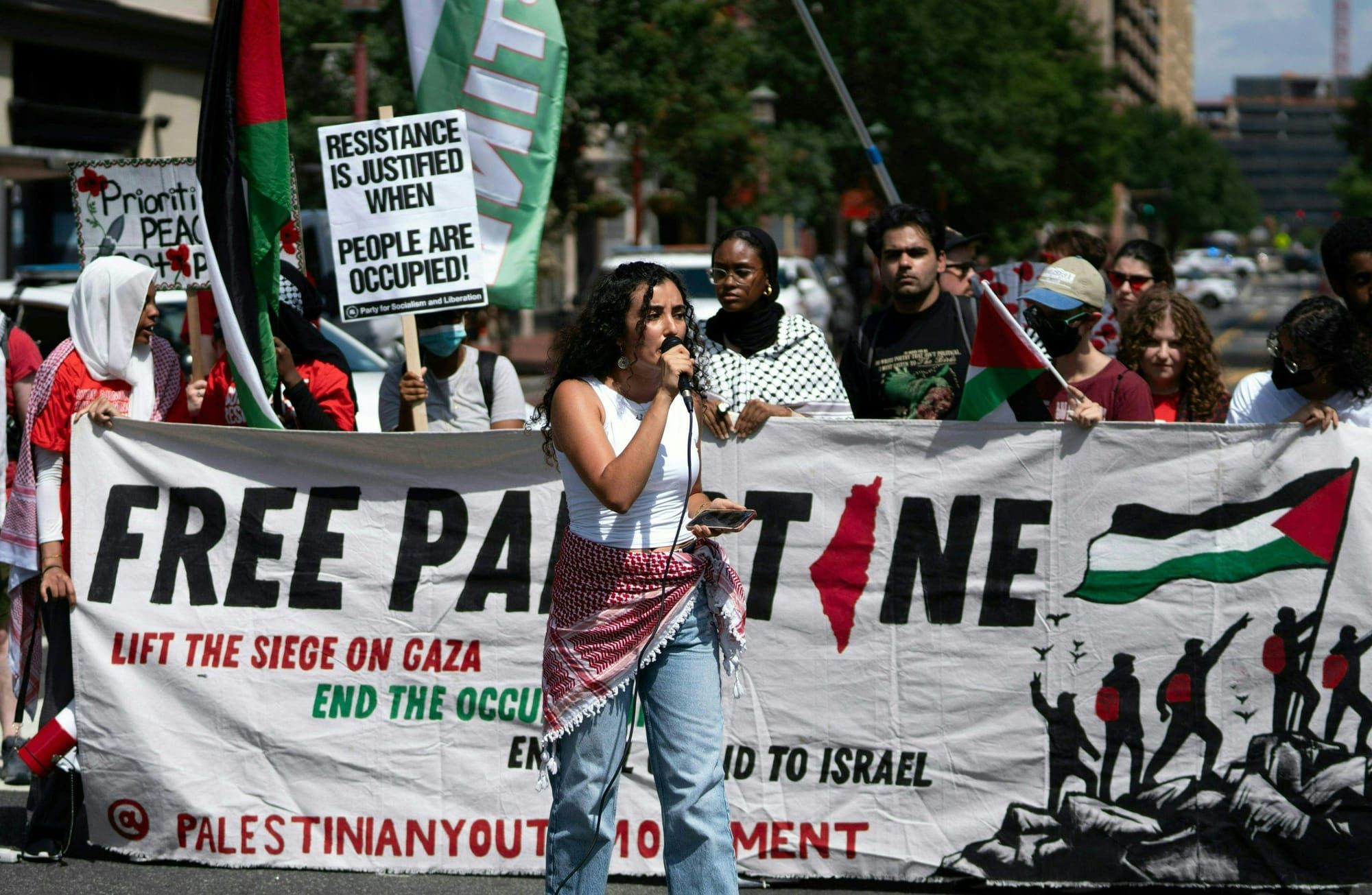 color photograph of an outdoor protest in support of Palestinian liberation. a fem person wearing jeans and a white tank top